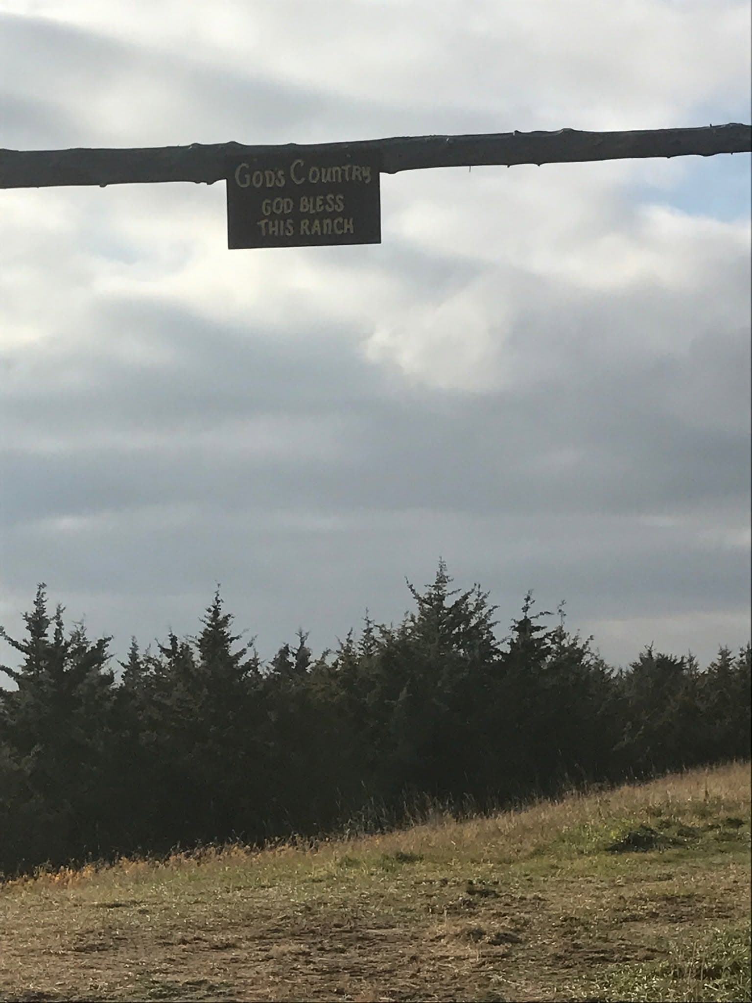Looking up at a hanging ranch sign on a timber gateway against a moody sky