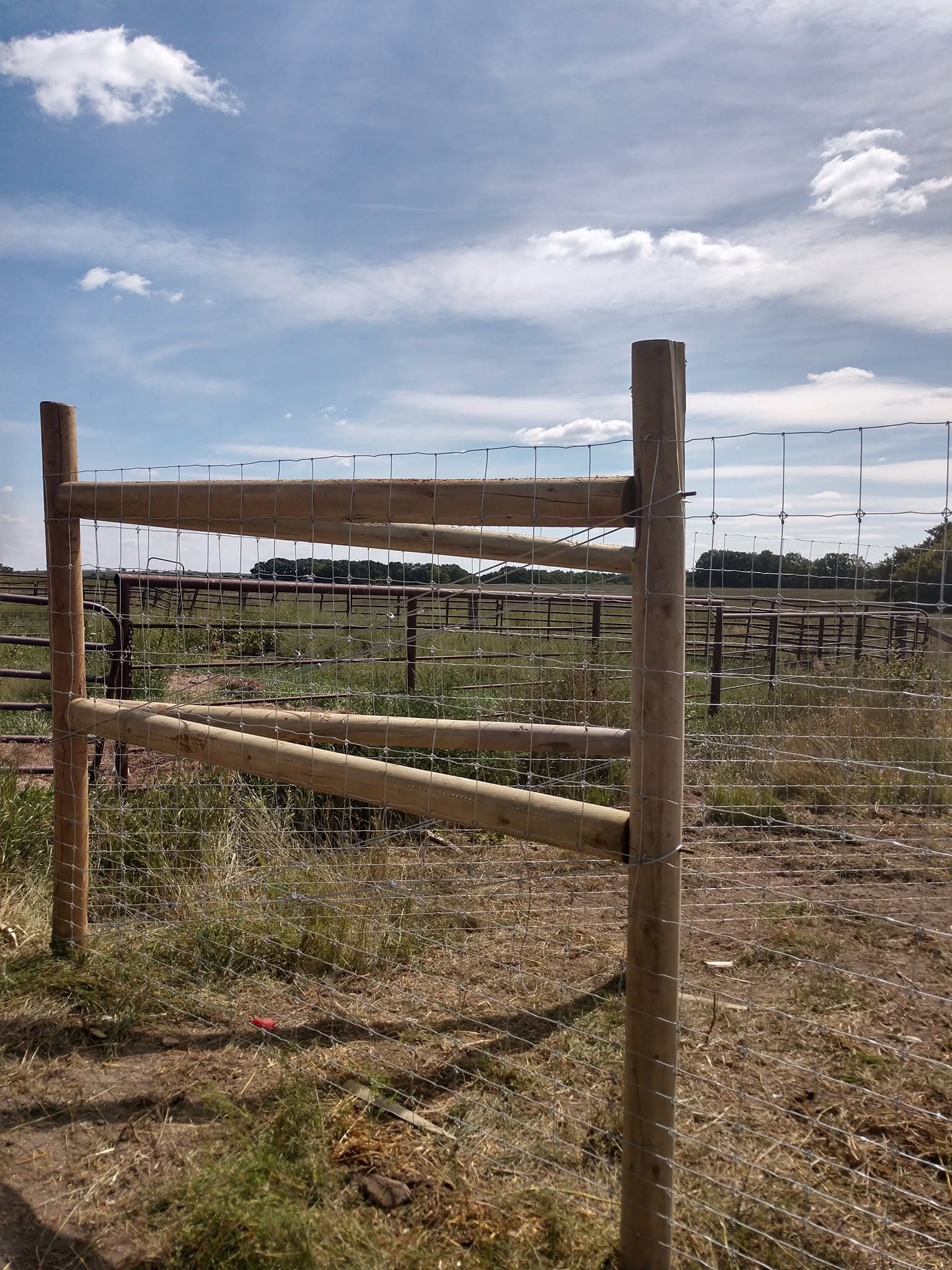 Doubled wood H-brace corner carrying woven wire beside a working corral