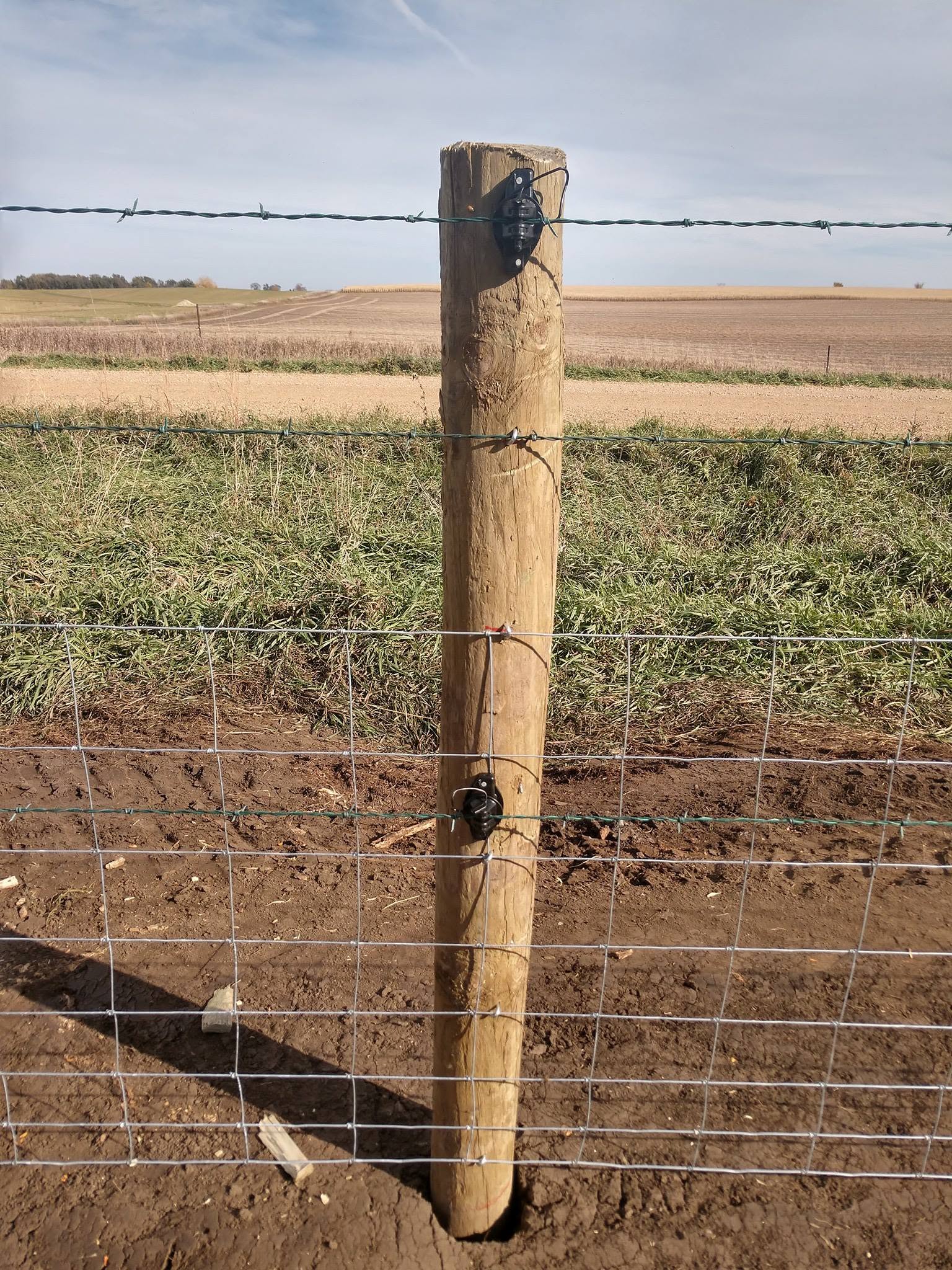 Woven field fence hung on a CCA treated post, twin coated barbed strands riding the top