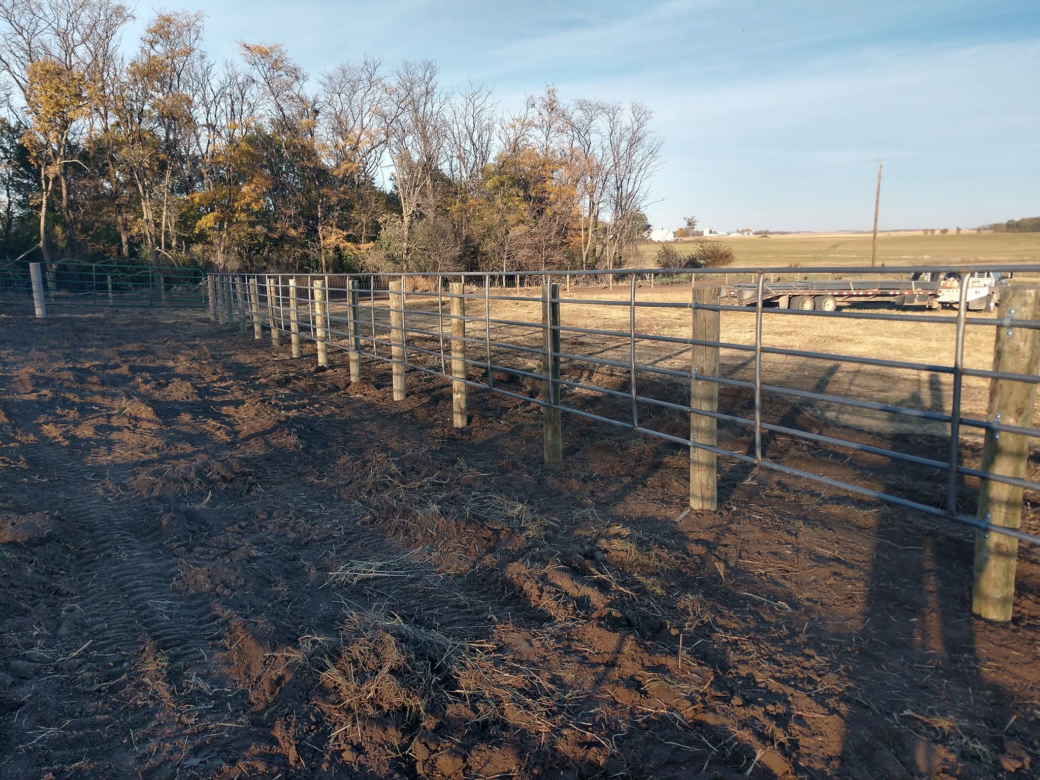 Rebuilt corral fence standing on fire-blackened ground with autumn trees behind
