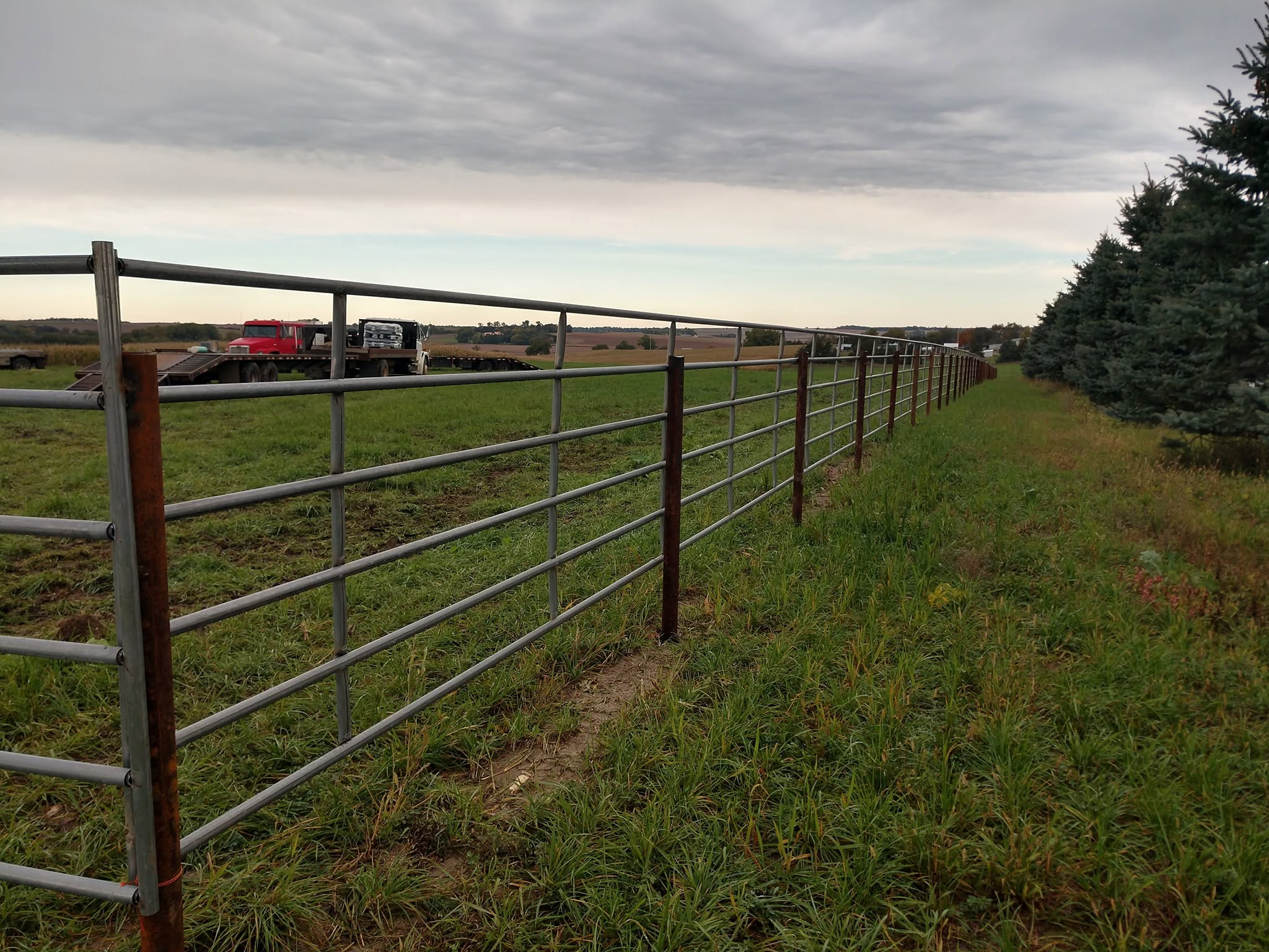 Continuous steel panel fence cornering across a farmstead yard