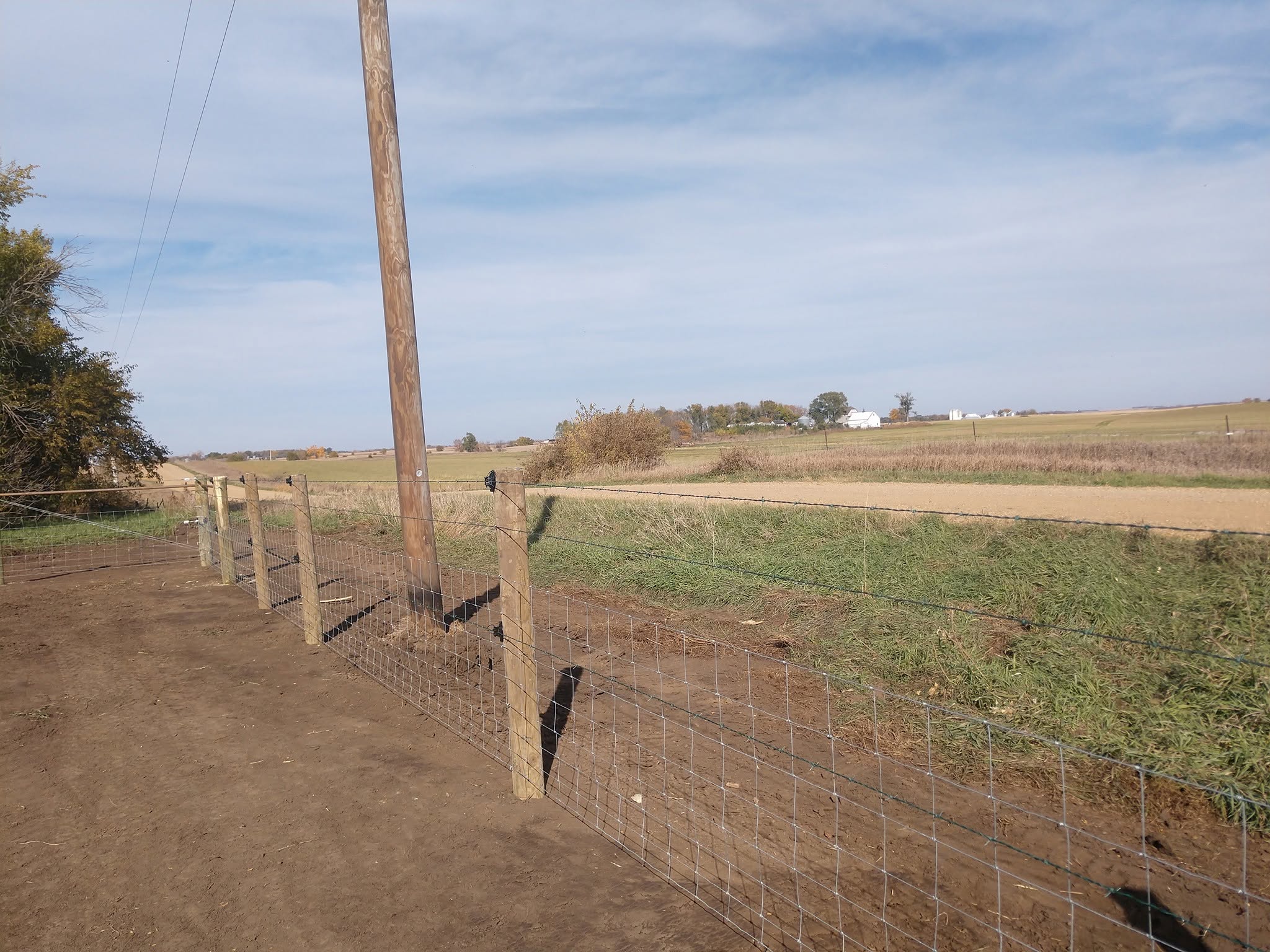 Tall wood post anchoring woven wire on open prairie