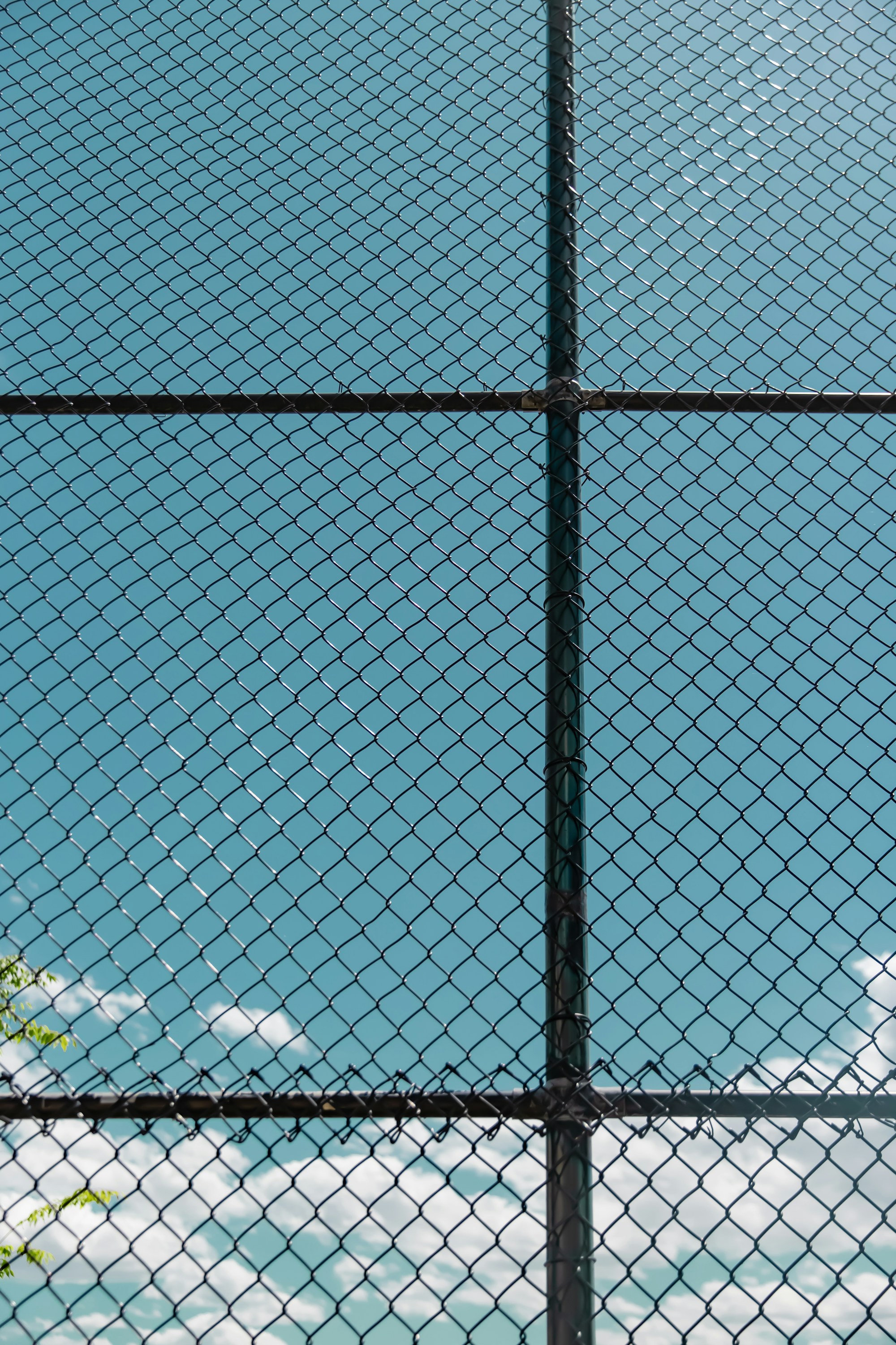 Black vinyl-coated chain-link fence on steel posts and rails against a blue sky